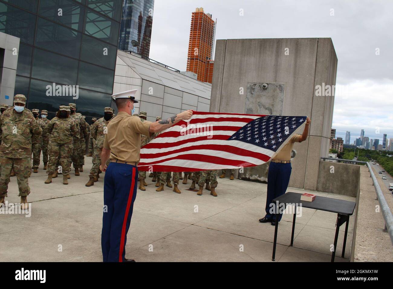 New York Naval Militia Service members (r) assigned to Joint Task Force Javits unfurl the American flag during a Memorial Day service held on the terrace of the Jacob K. Javits Center in Manhattan, New York on Monday May 31, 2021. Over 3,180 members of the New York Army and Air National Guard, the New York Naval Militia and the New York Guard are supporting the multi-agency response to COVID-19 at 24 vaccination sites and other locations across New York. Stock Photo