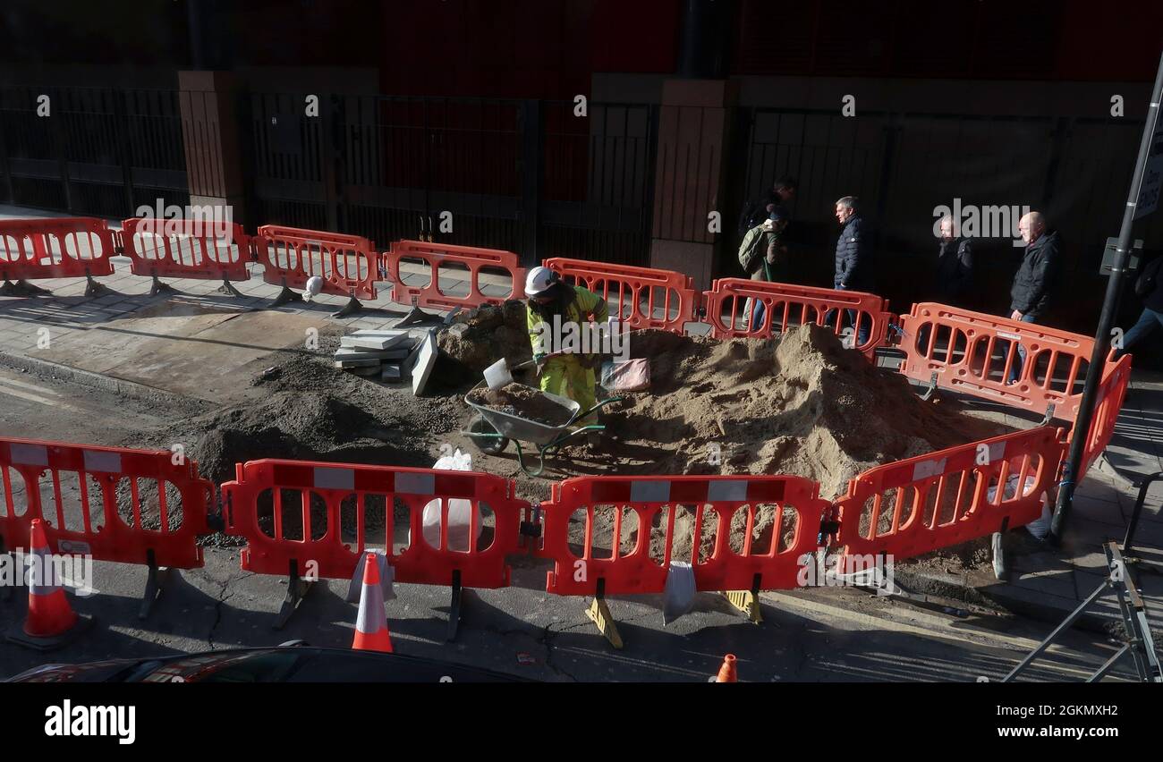 Pedestrians walk past plastic barriers around road construction work in Central London, UK Stock Photo