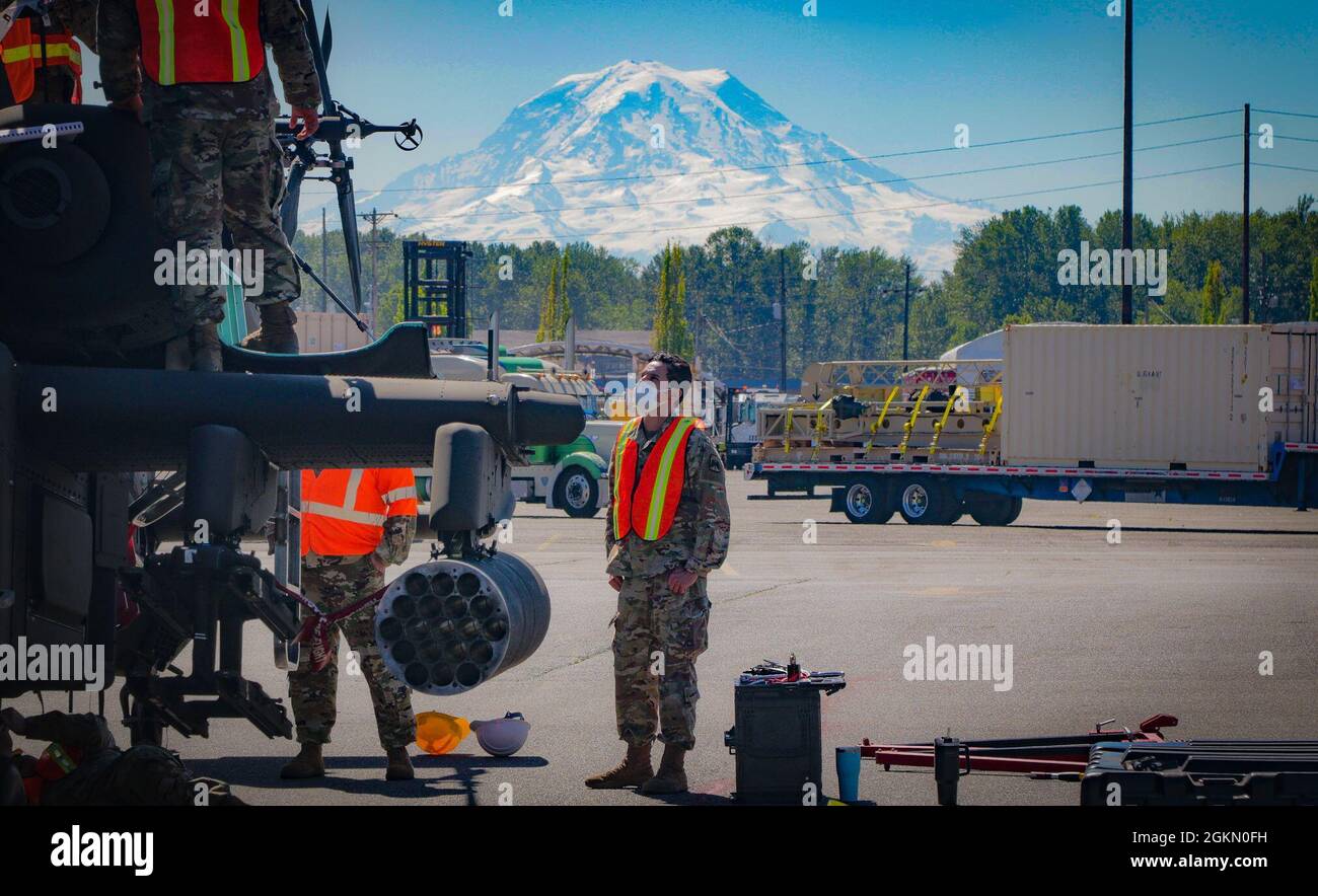 Soldiers assigned to 46th Aviation Support Battalion, 16th Combat Aviation Brigade, prepare an AH-64 attack helicopter for shipment at the Port of Tacoma, Wash., on Jun. 1, 2021.  The unit was preparing aircraft and equipment to be loaded onto a vessel for transport to a training exercise.  Mount Rainier is visible in the background. Stock Photo