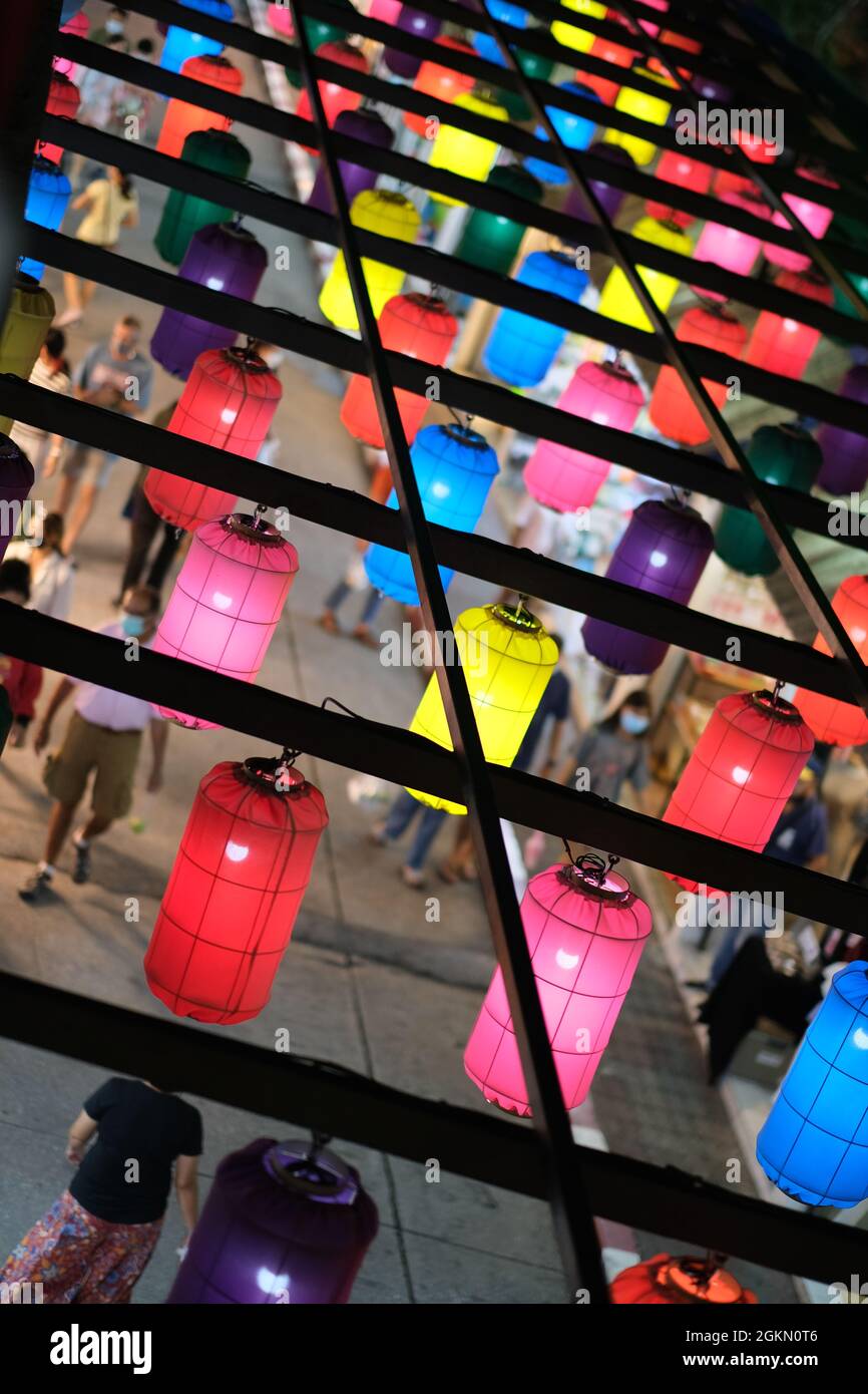 People are wandering through night street market under the canopy of colorful lanterns Stock Photo