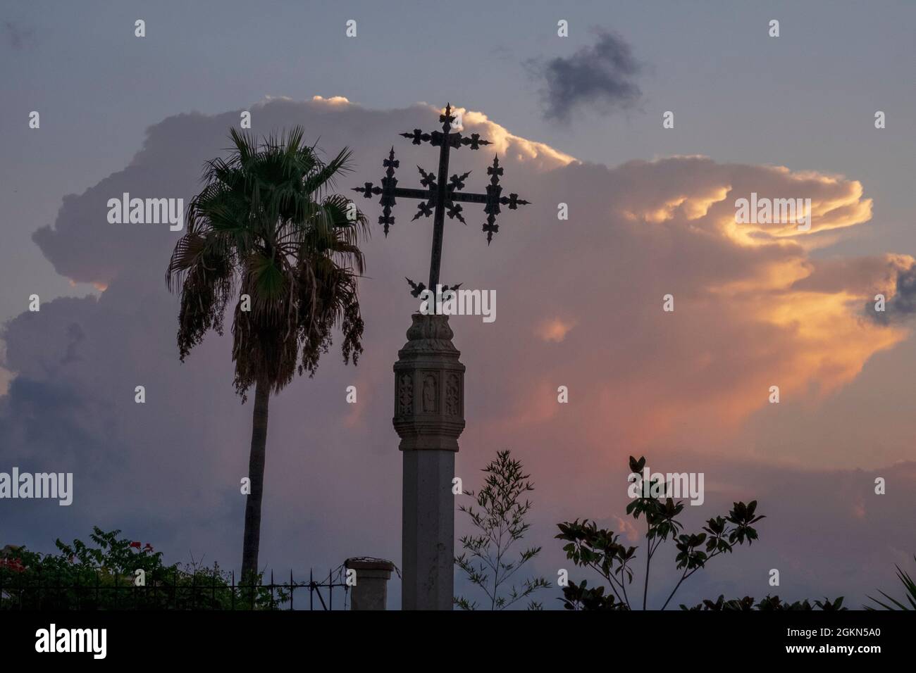 Cross and palm tree against a storm cloud in the morning sky, Selva, Mallorca, Spain Stock Photo