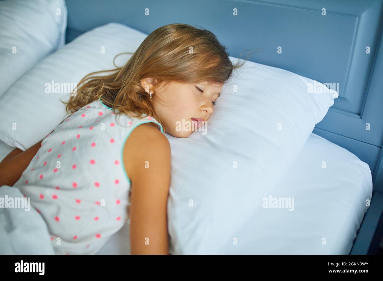 Little girl sleeping on a big and cozy bed white linen in the afternoon ...