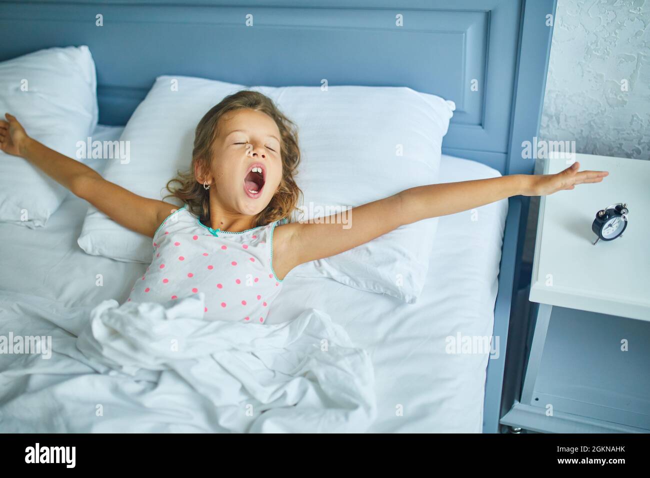 Little girl wakes up from sleep on a big and cozy bed white linen