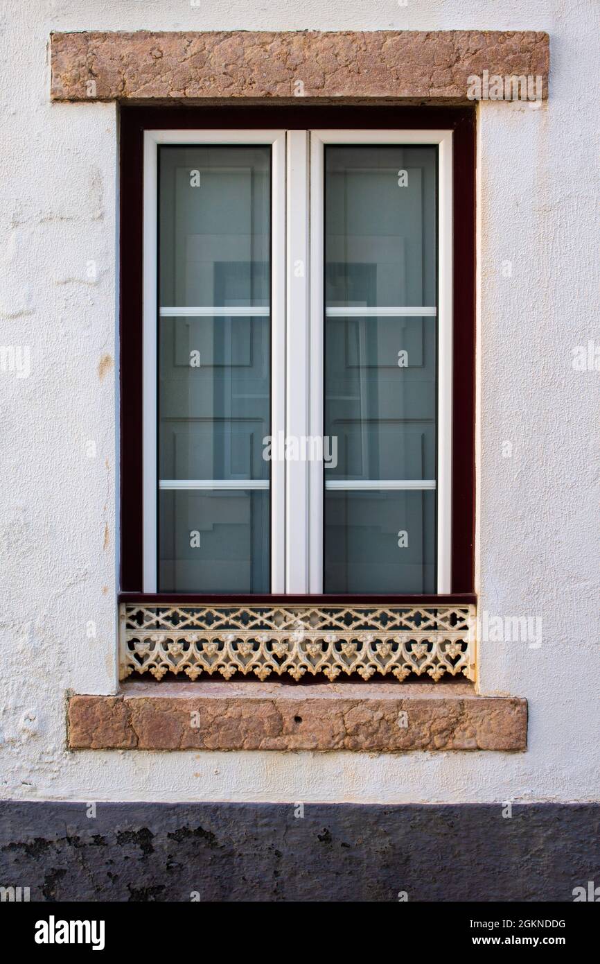 Restored traditional old window in Portuguese neighbourhood with white and red frame and carved metal guard Stock Photo