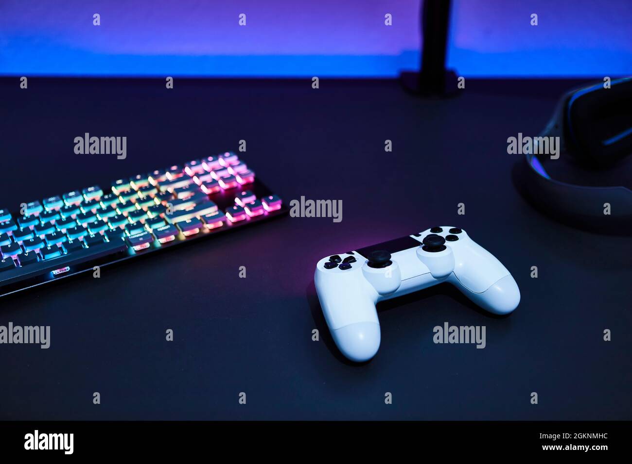 White game controller, color backlighted keyboard and headphones on grey desk. Professional computer game playing, esport business and online world co Stock Photo