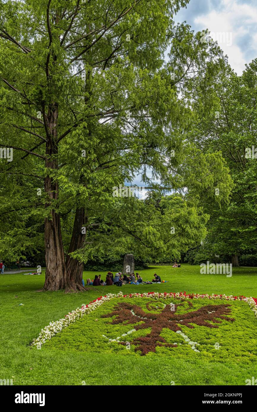 Group of young people sitting on the grass in the shade of a tree in the landscaped gardens of the imperial palace. Innsbruck, Tyrol, Austria, Europe Stock Photo