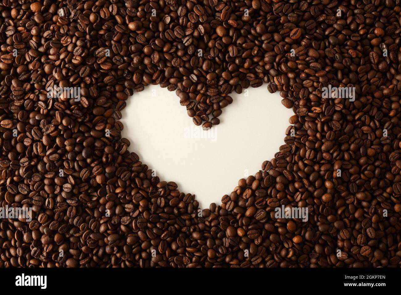 Pile of coffee beans with hollow on a white table forming the shape of a heart. Top view. Horizontal composition. Stock Photo