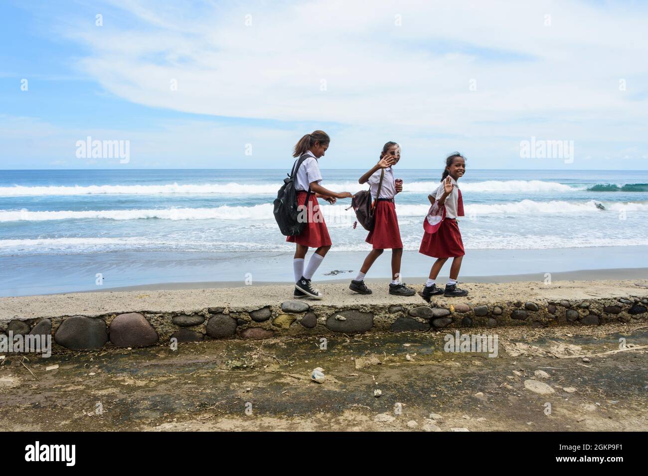 Three joyous school girls in red and white school uniforms returning home from school. Sikka village, Flores island, East Nusa Tenggara, Indonesia. Stock Photo