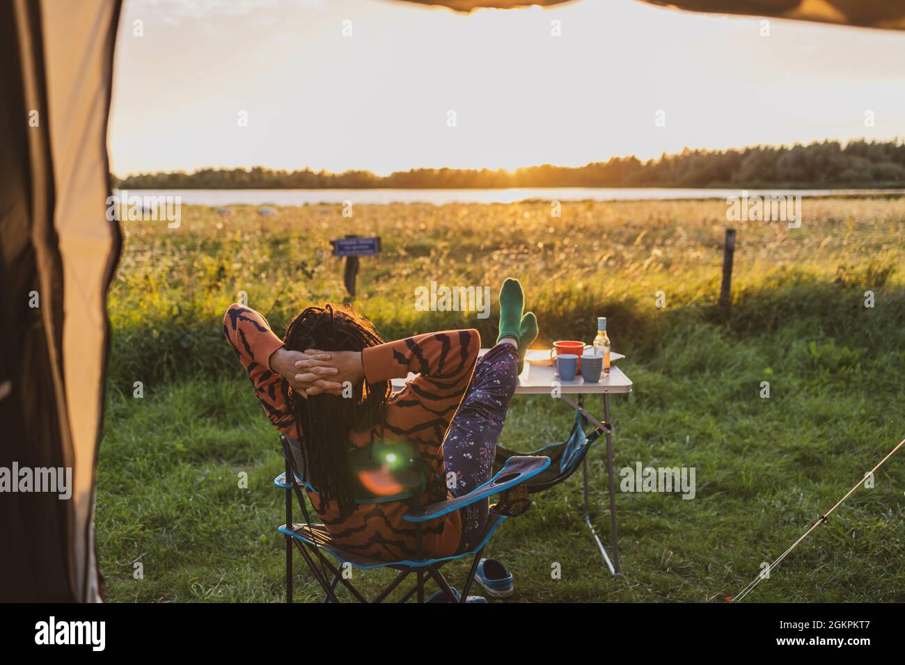 Woman relaxing in front of the tent during sunset Stock Photo