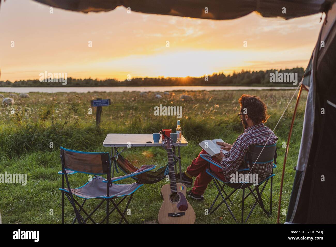 Man reading a book at a campsite. View from a tent Stock Photo
