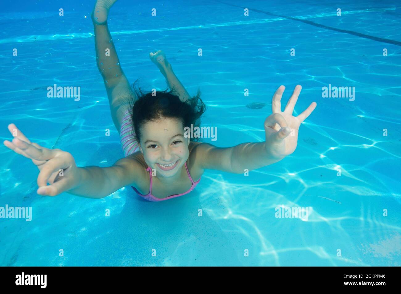 Young girl of 7 swimming underwater gives the OK hand gesture Stock Photo