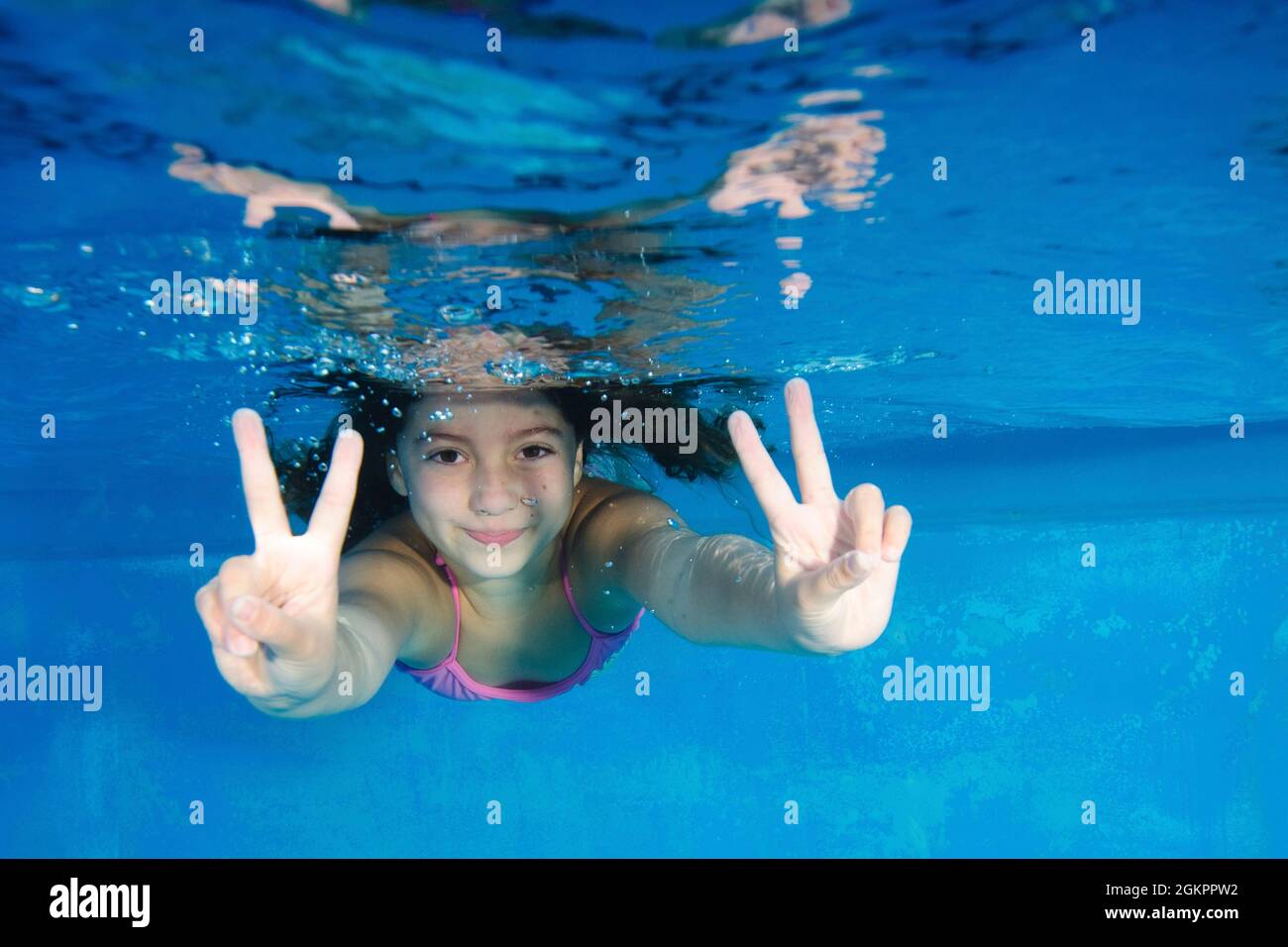 Young girl of 7 swimming underwater gives the Thumbs up sign Stock Photo
