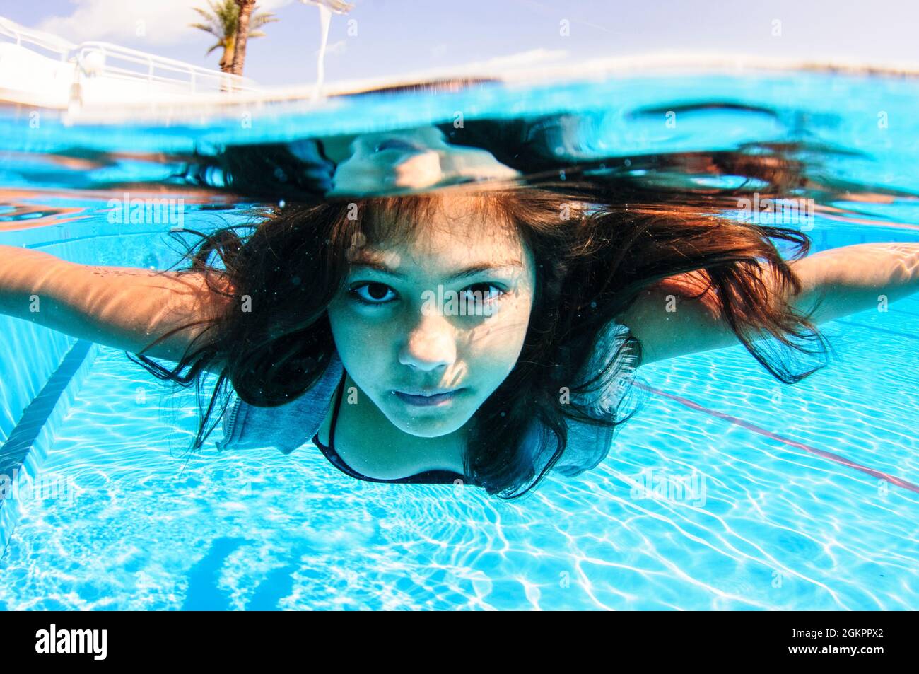 A dressed 12 year old female teen free diving under water in a swimming pool. Model release available Stock Photo