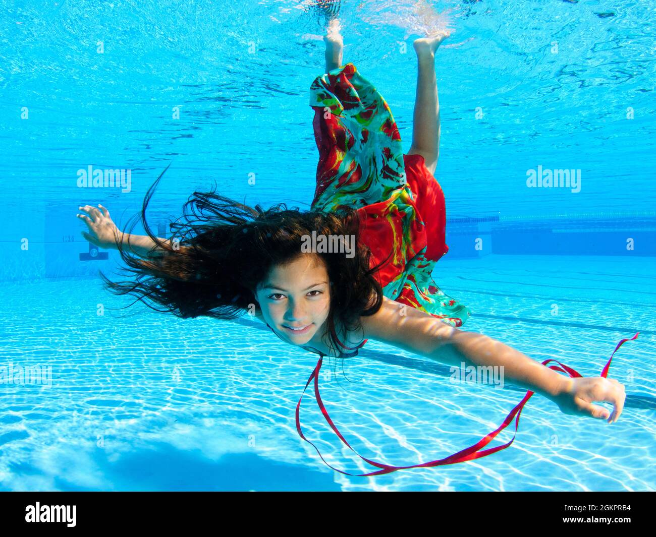 A 12 year old female teen dressed in colourful dress free diving underwater in a swimming pool. Model release available Stock Photo