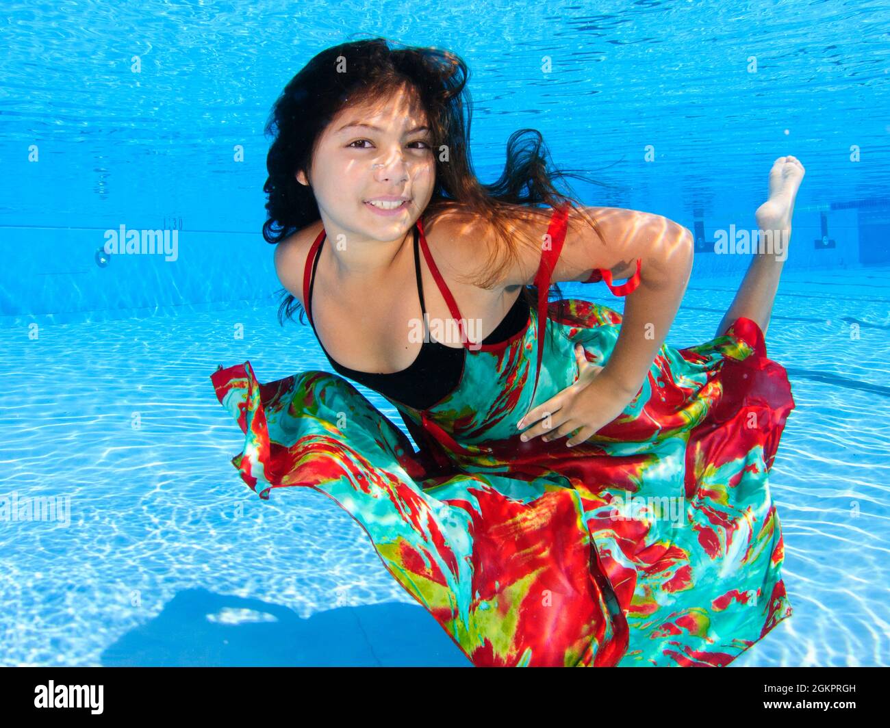 A 12 year old female teen dressed in colourful dress free diving underwater in a swimming pool. Model release available Stock Photo