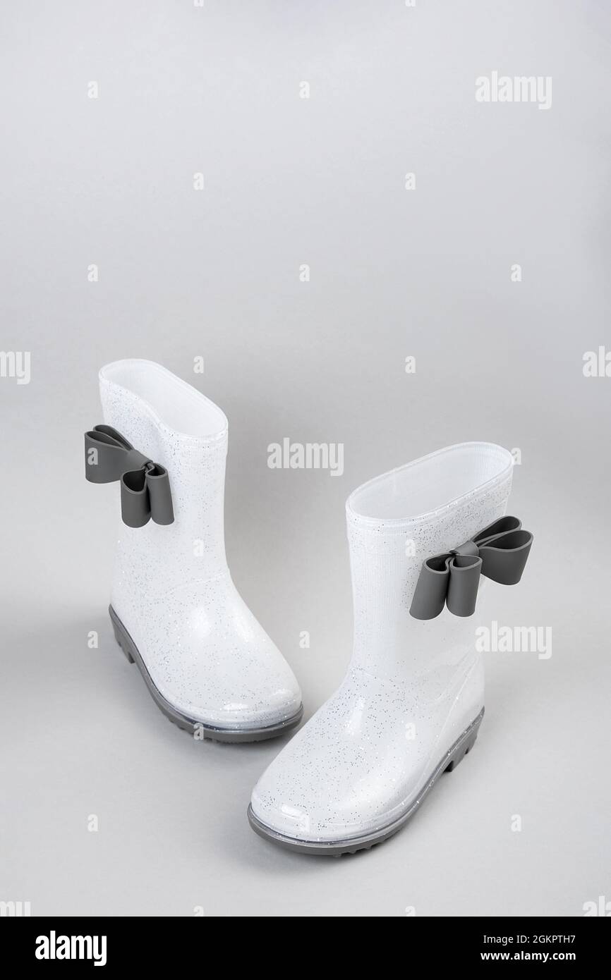 White shiny rubber rain boots with bows on gray background with copy