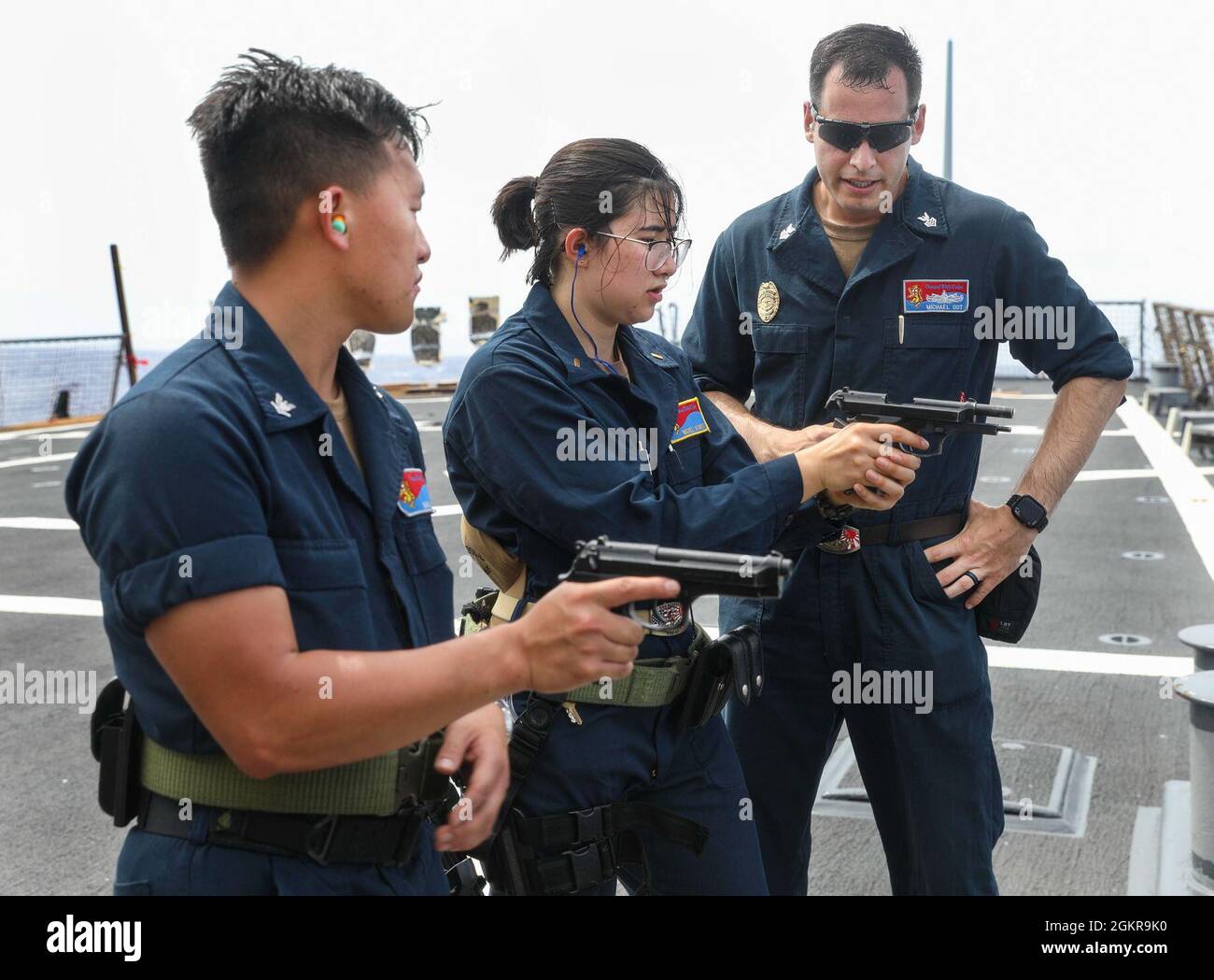 Master at Arms 1st Class Michael Oot, from Syracuse, N.Y., gives weapon familiarization training to Fire Controlman (Aegis) 3rd Class Nhia Her, from Saint Paul, Minn, and Ens. Nicole Schiff, from Silver Springs, Md., during a small arms qualification aboard Arleigh Burke-class guided-missile destroyer USS Benfold (DDG 65). Benfold is assigned to Commander, Task Force (CTF) 71/Destroyer Squadron (DESRON) 15, the Navy’s largest forward-deployed DESRON and the U.S. 7th Fleet’s principal surface force. Stock Photo