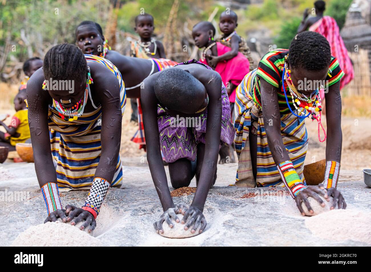 Young girls grinding Sorghum on a rock, Laarim tribe, Boya Hills, Eastern Equatoria, South Sudan, Africa Stock Photo