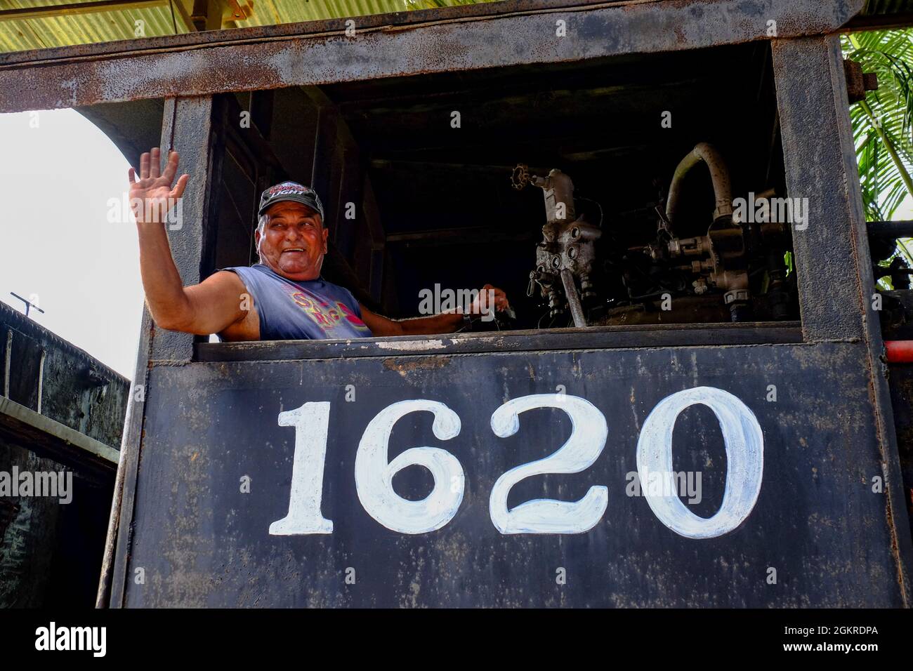 A smiling man waves from the engine of a train, Cienfuegos, Cuba, West Indies, Central America Stock Photo