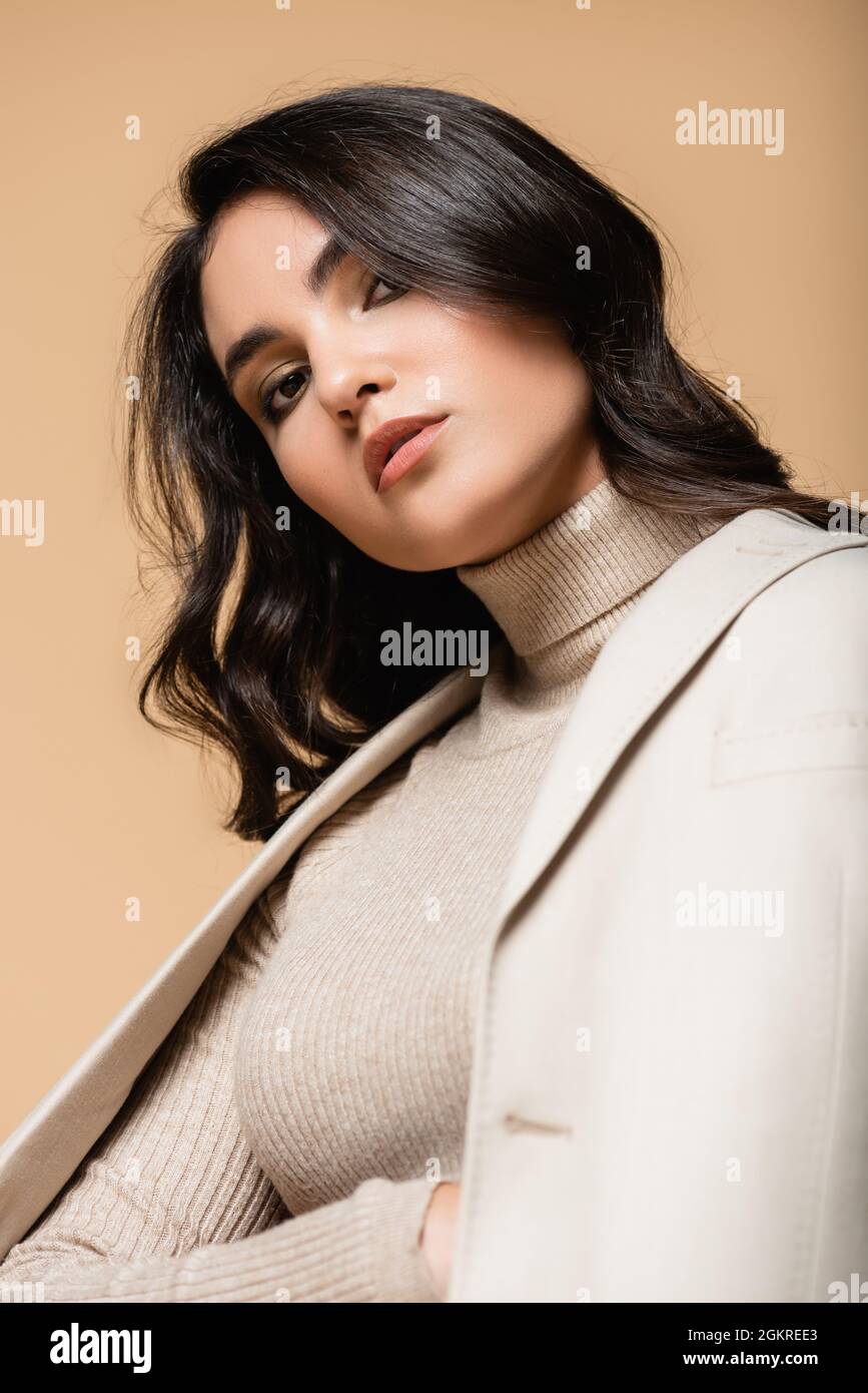 young pretty model in turtleneck and blazer looking at camera isolated on beige Stock Photo