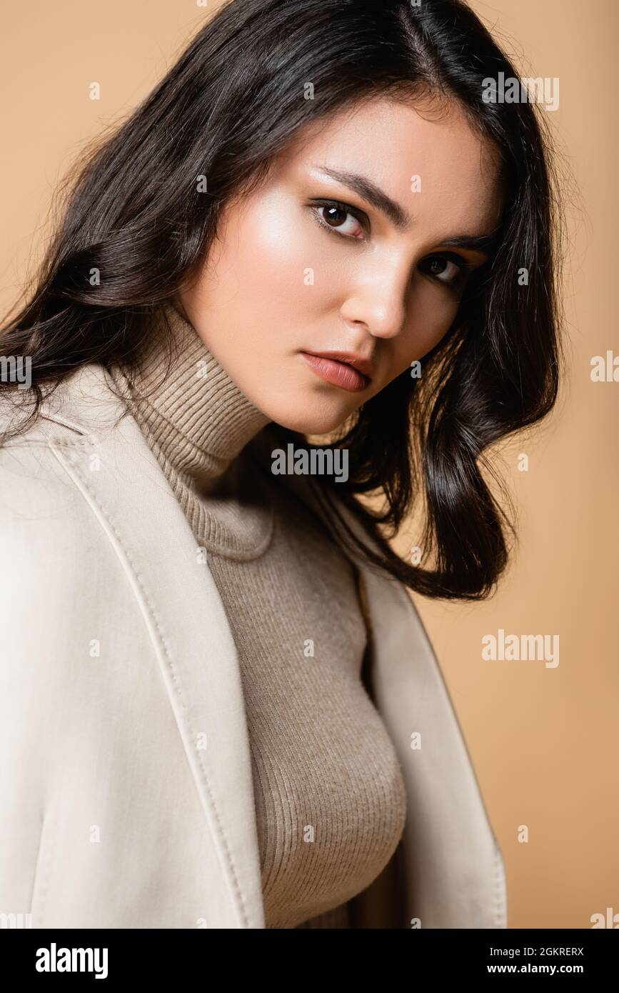 brunette and pretty model in turtleneck looking at camera isolated on beige Stock Photo