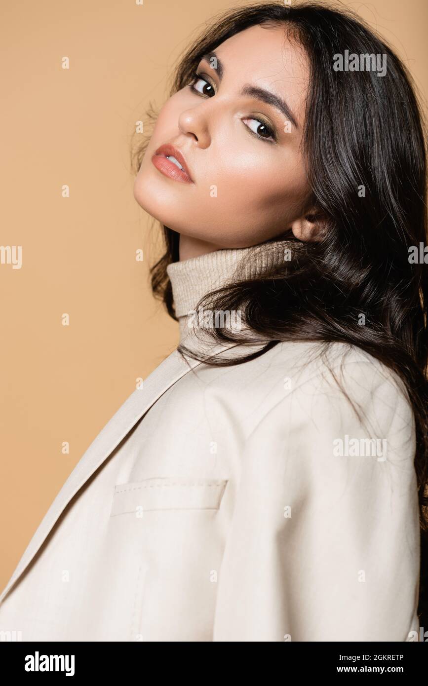 pretty model in turtleneck and blazer looking at camera isolated on beige Stock Photo