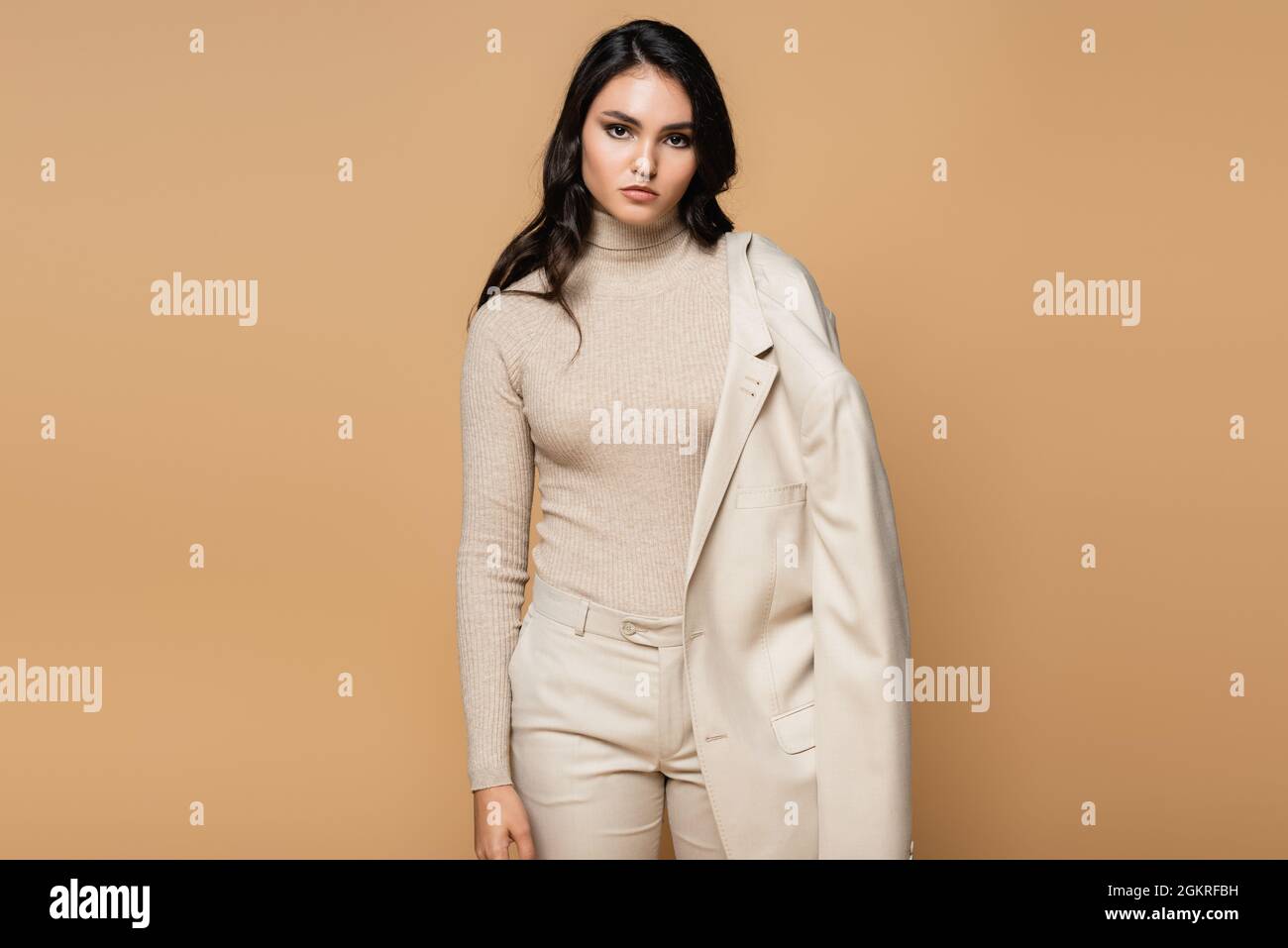 pretty model in turtleneck holding blazer and posing isolated on beige Stock Photo