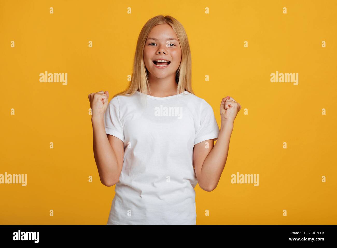 Happy excited teenager blonde girl pupil in white t-shirt rejoices victory and gestures Stock Photo