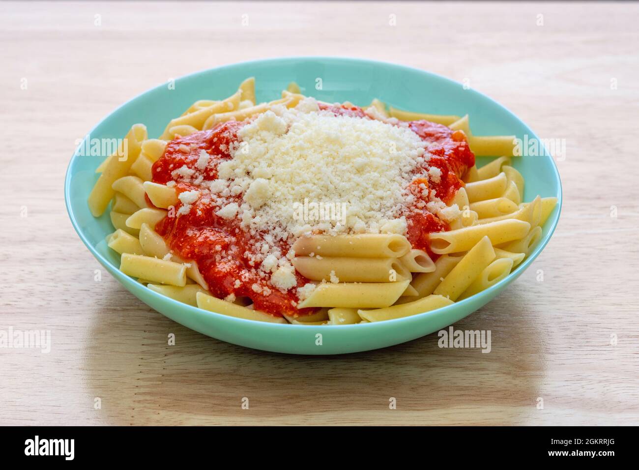 Blue deep plate filled with macaroni with bolognese sauce and grated parmesan cheese galore on pine wood table Stock Photo