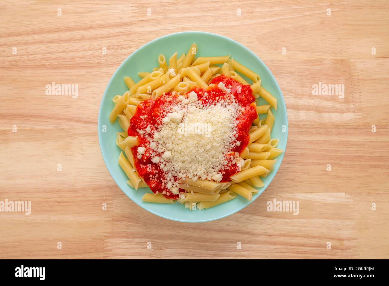 Top view image of cooked macaroni with tomato sauce and parmesan cheese on blue plate and wooden table Stock Photo