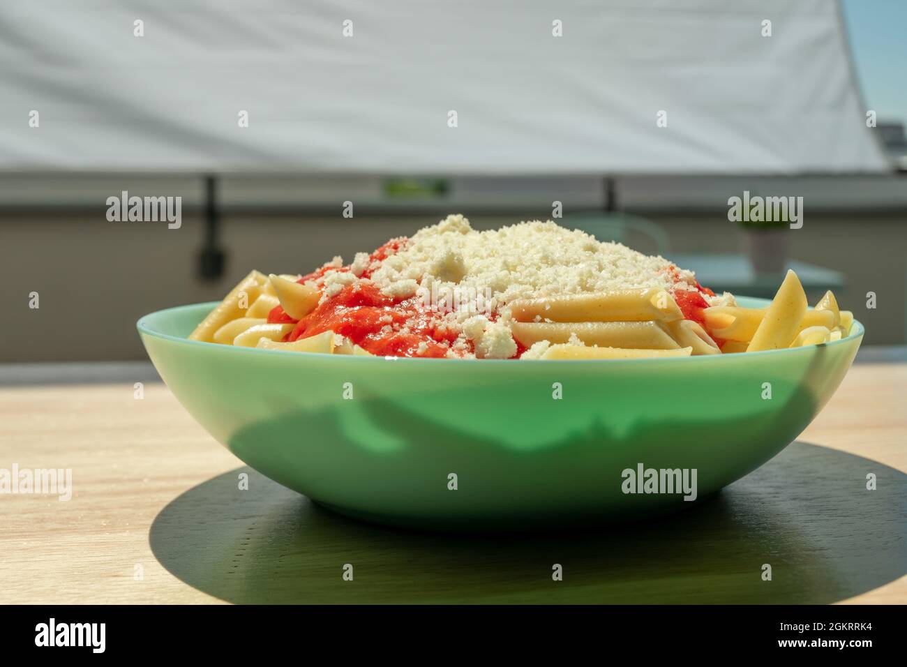 blue deep plate with macaroni with tomato and grated cheese on wooden table in the sun Stock Photo