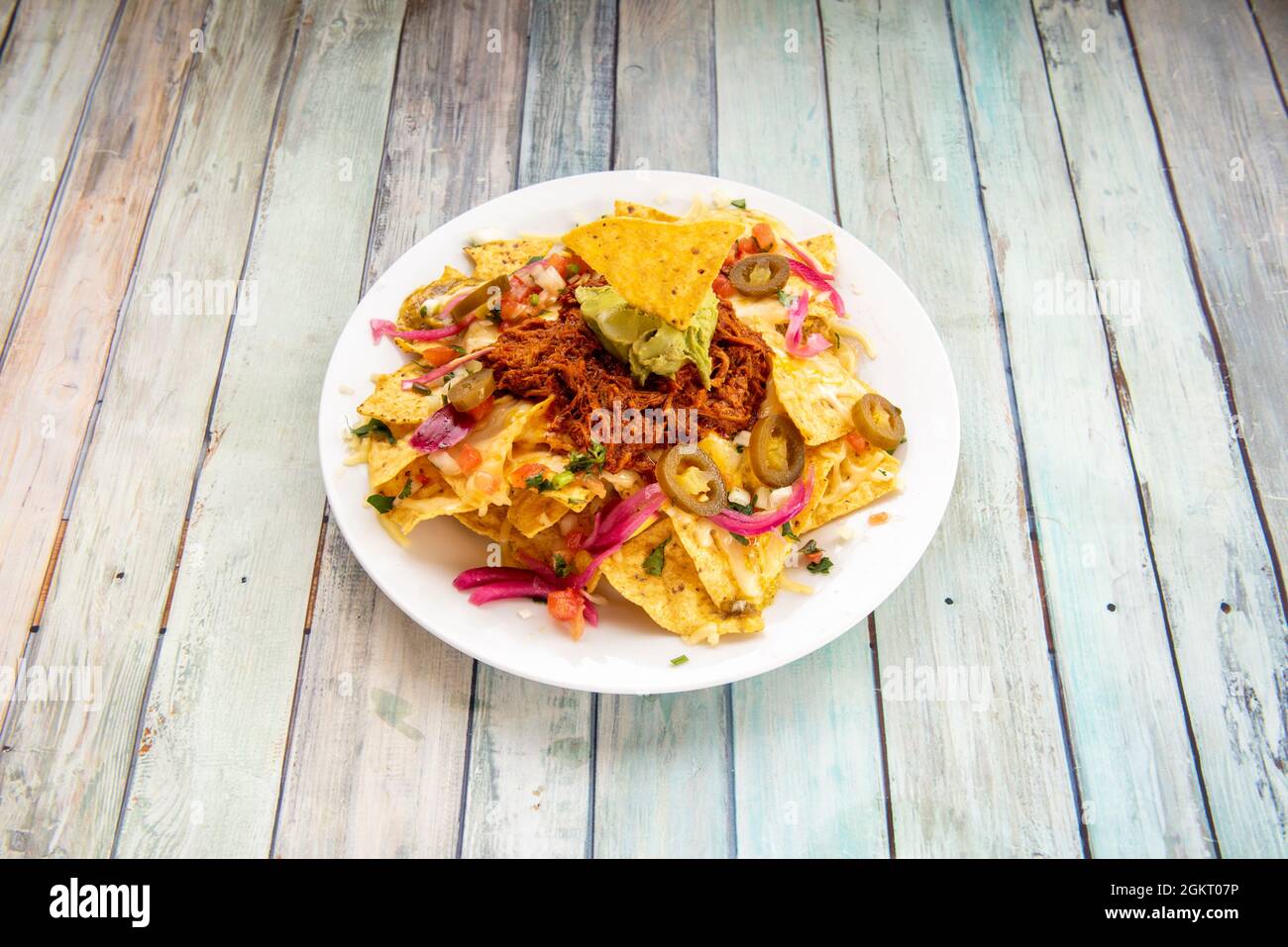 Mexican corn nachos with avocado guacamole, cochinita pibil meat and sliced jalapenos on white plate Stock Photo