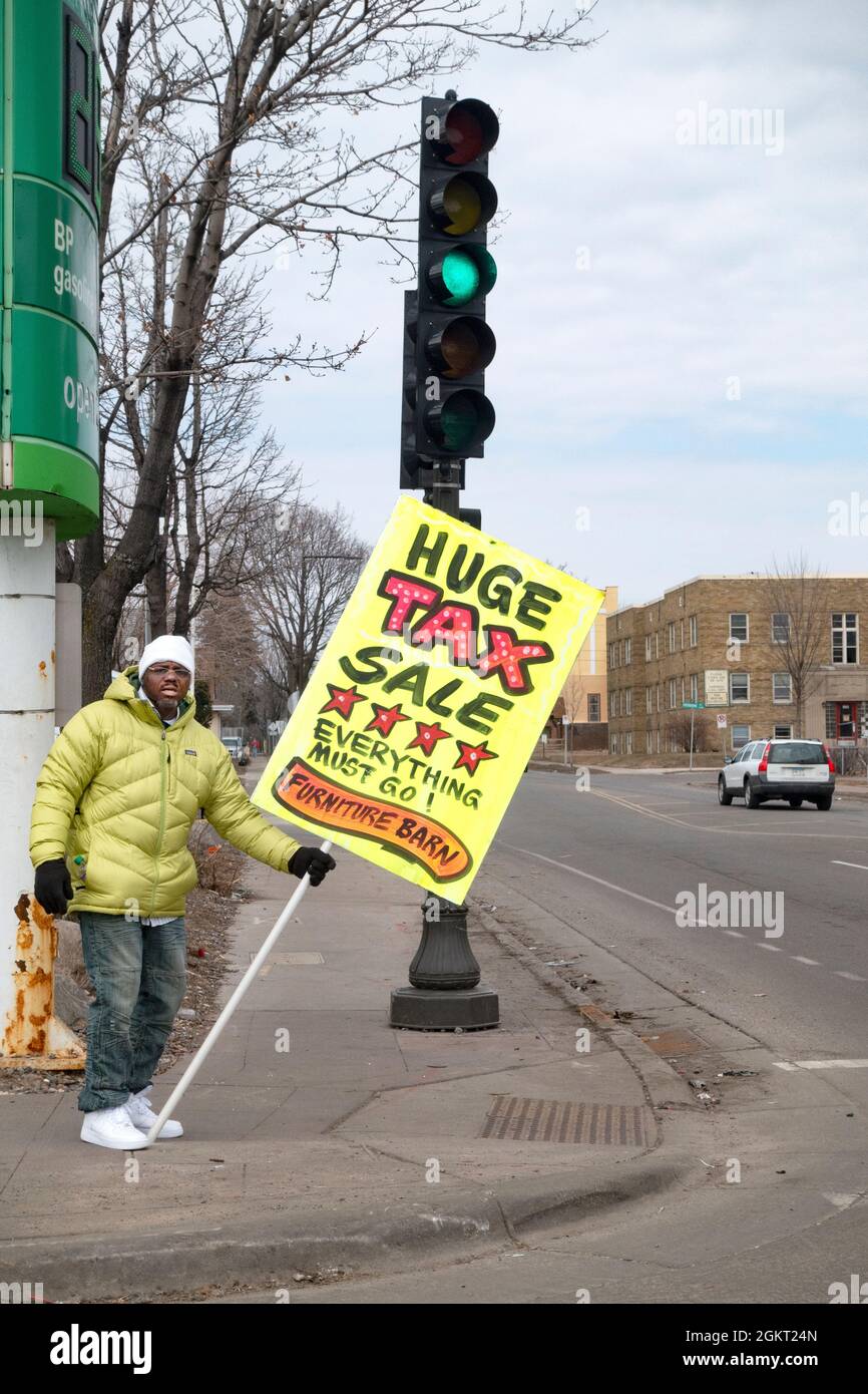 Man on the corner holding a sign for a tax sale at the Furniture Barn. St Paul Minnesota MN USA