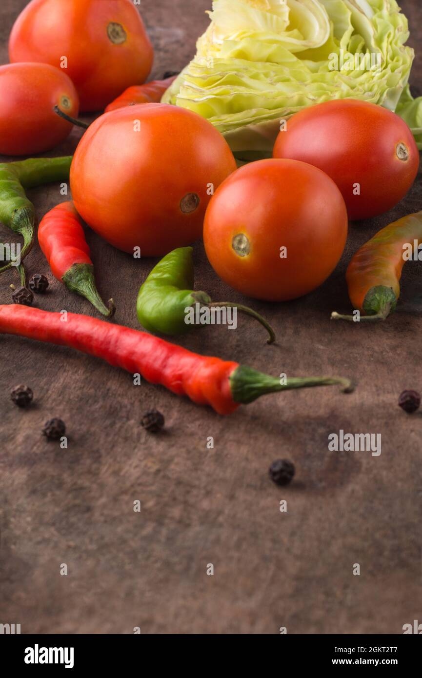organic vegetables on a wooden surface, tomatoes, green and red chilies, cabbage with black peppers, closeup view with copy space taken in shallow de Stock Photo