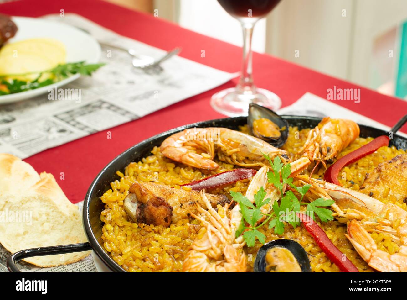 Mixed Valencian paella for two with stewed chicken, red pepper, saffron, prawns, crayfish and mussels and a glass of red wine Stock Photo