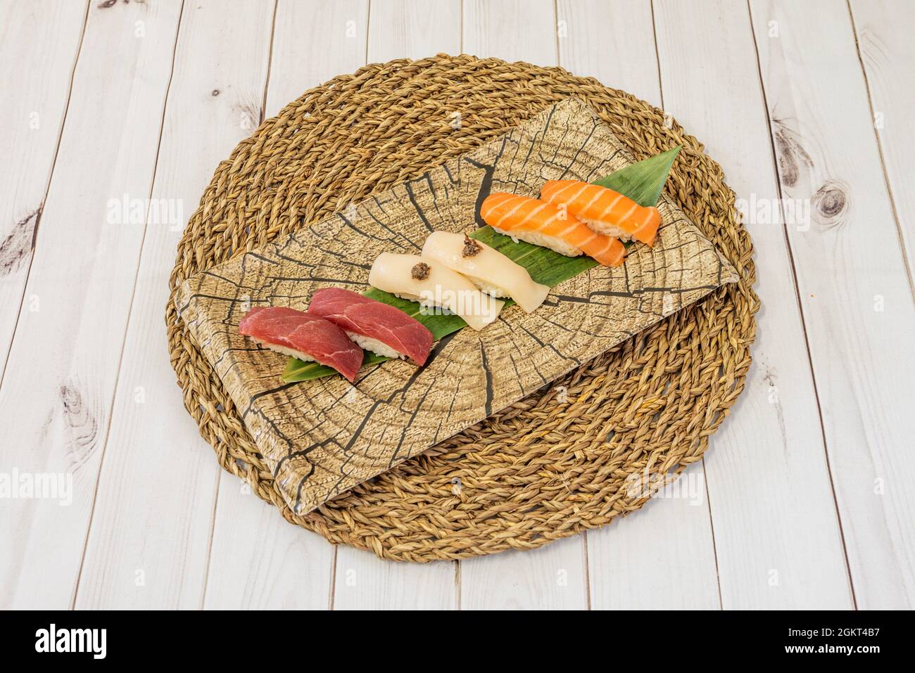 Plate of tuna, butterfish and salmon nigiri on wicker trivet and white