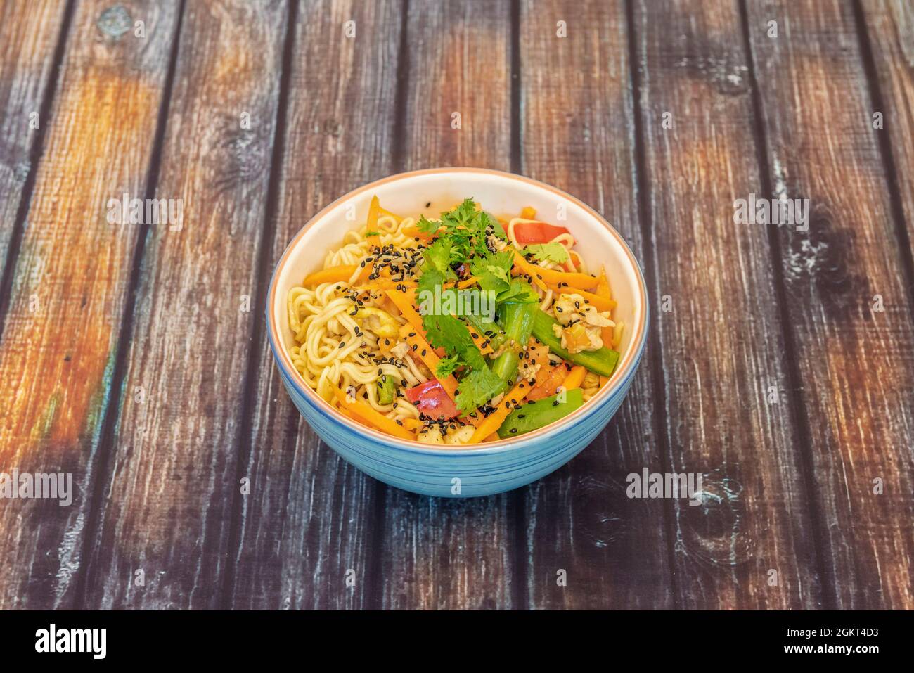 blue bowl of spaghetti with vegetables, coriander, poppy seeds and sesame Stock Photo