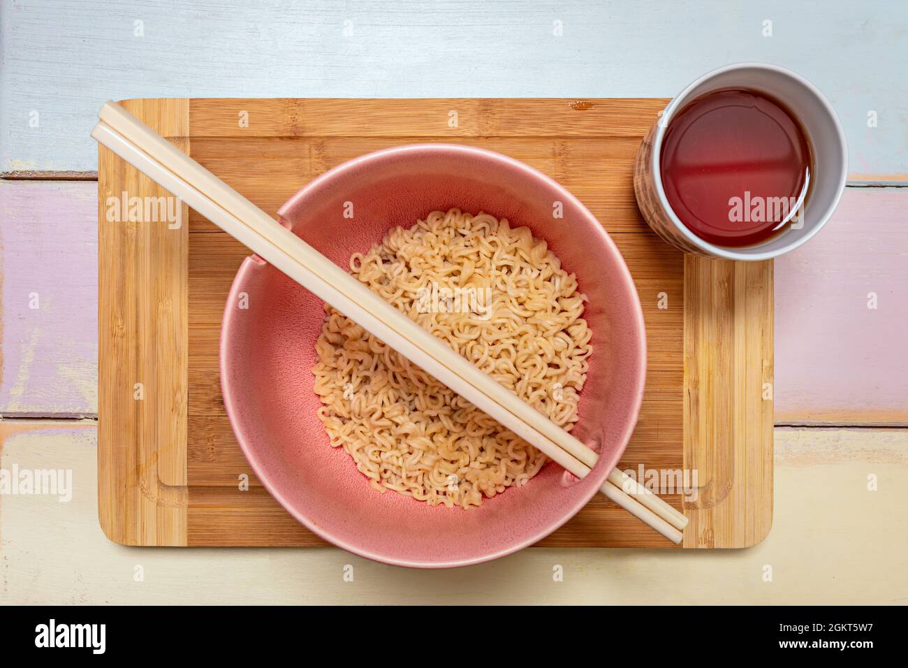 Top view image of pink bowl with Chinese curly noodles, chopsticks and red tea glass Stock Photo