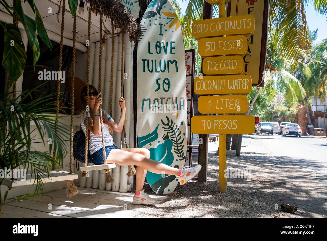 Woman sitting on swing seat of coconut shop with drink menu at roadside