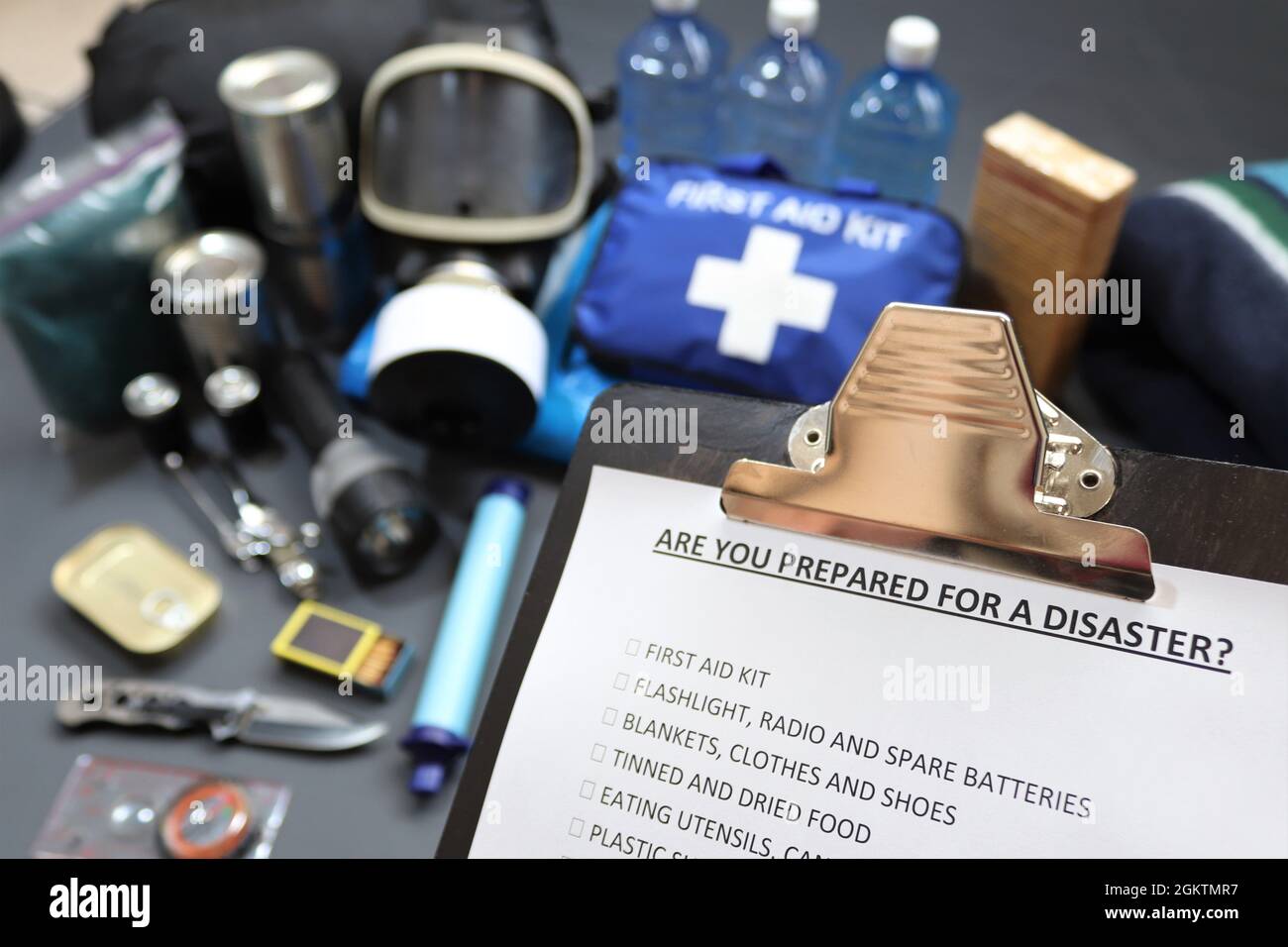 Disaster preparedness checklist on a clipboard with disaster relief items in the background.Such items would include a first aid kit,flashlight,ect Stock Photo