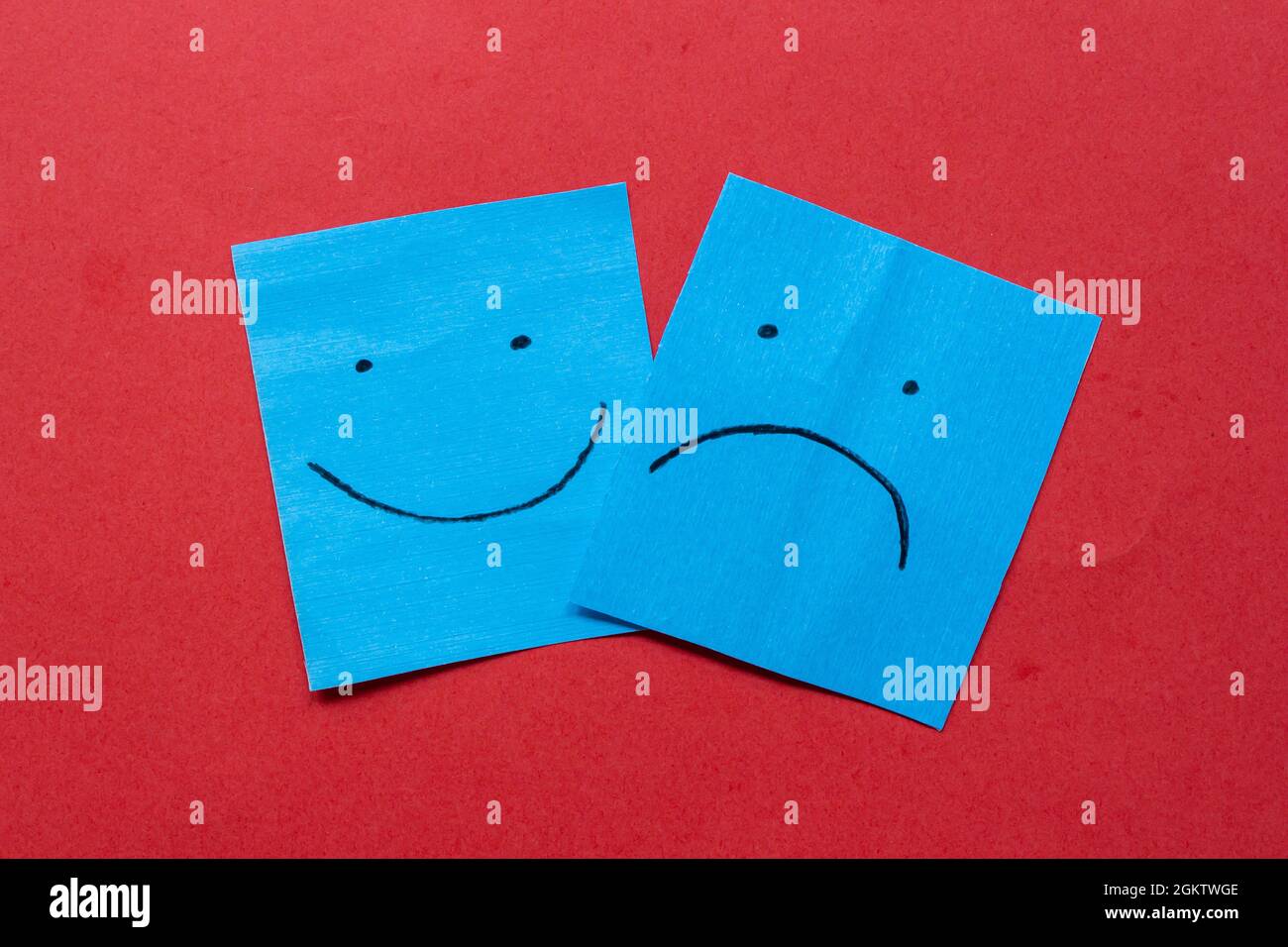 Happy and sad face on stickers. Hand drawn faces on paper. Different emotions together. Isolated on red background. Stock Photo