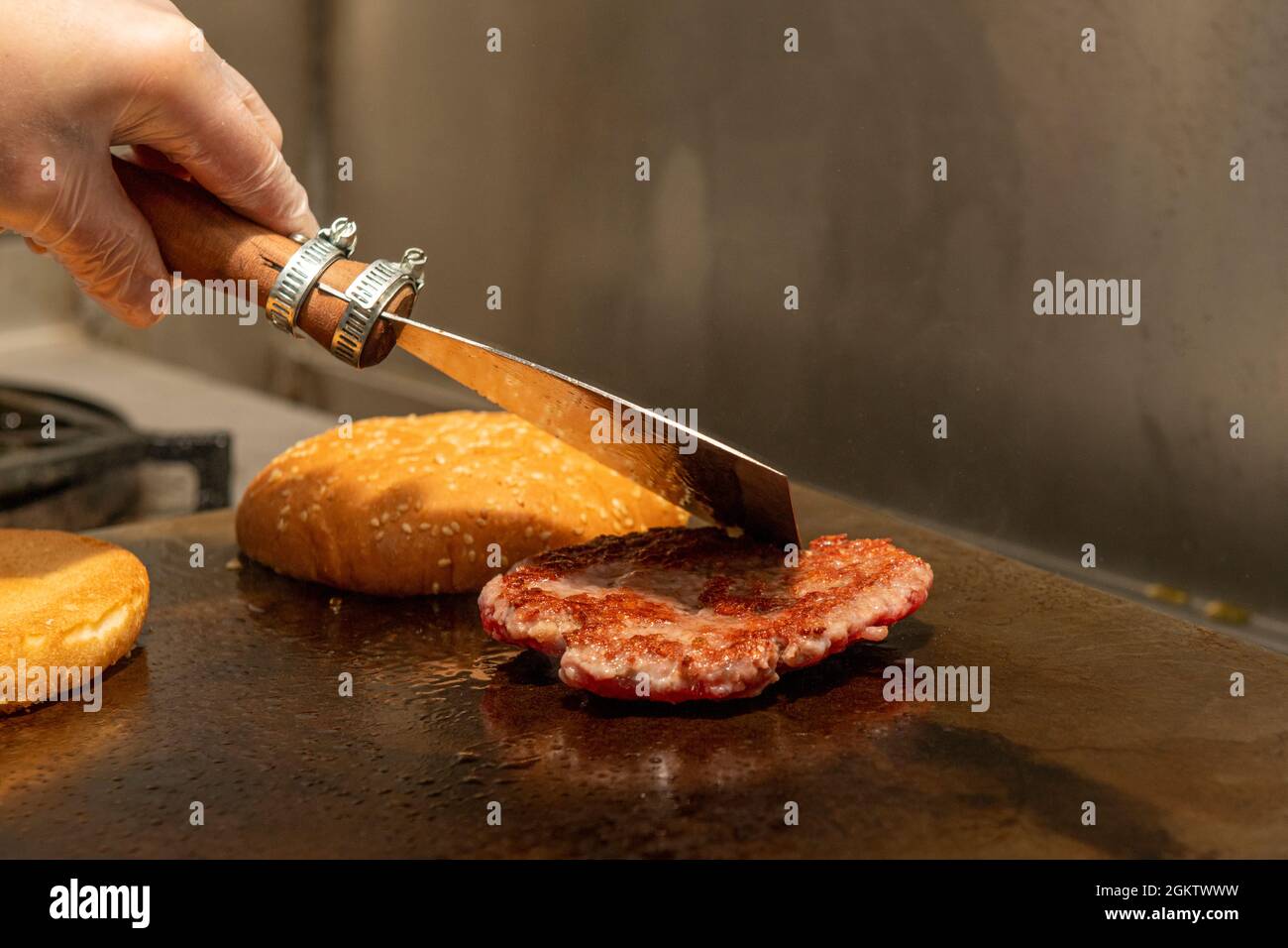 Chef's left hand handling a spatula to cook a grilled hamburger in a restaurant kitchen Stock Photo