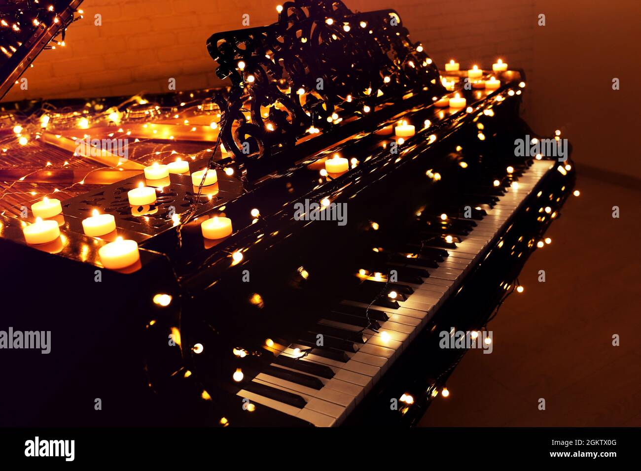 Vintage piano with Christmas lights and candles in dark room Stock