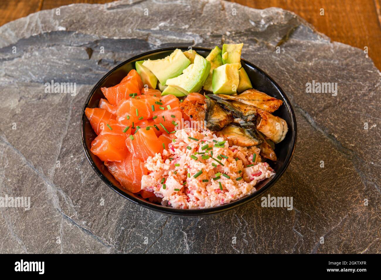 Black fish poke bowl, surimi, diced salmon, green avocado and pieces of stewed eels on gray stone Stock Photo