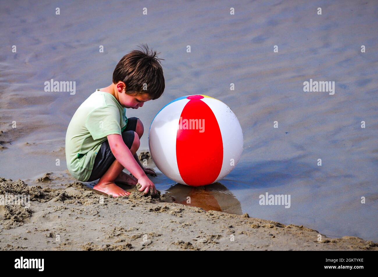 A little boy hears the call,"time to go home." When mother calls the dream of little boys is over, the fun of playing with a stone in a puddle end. Stock Photo