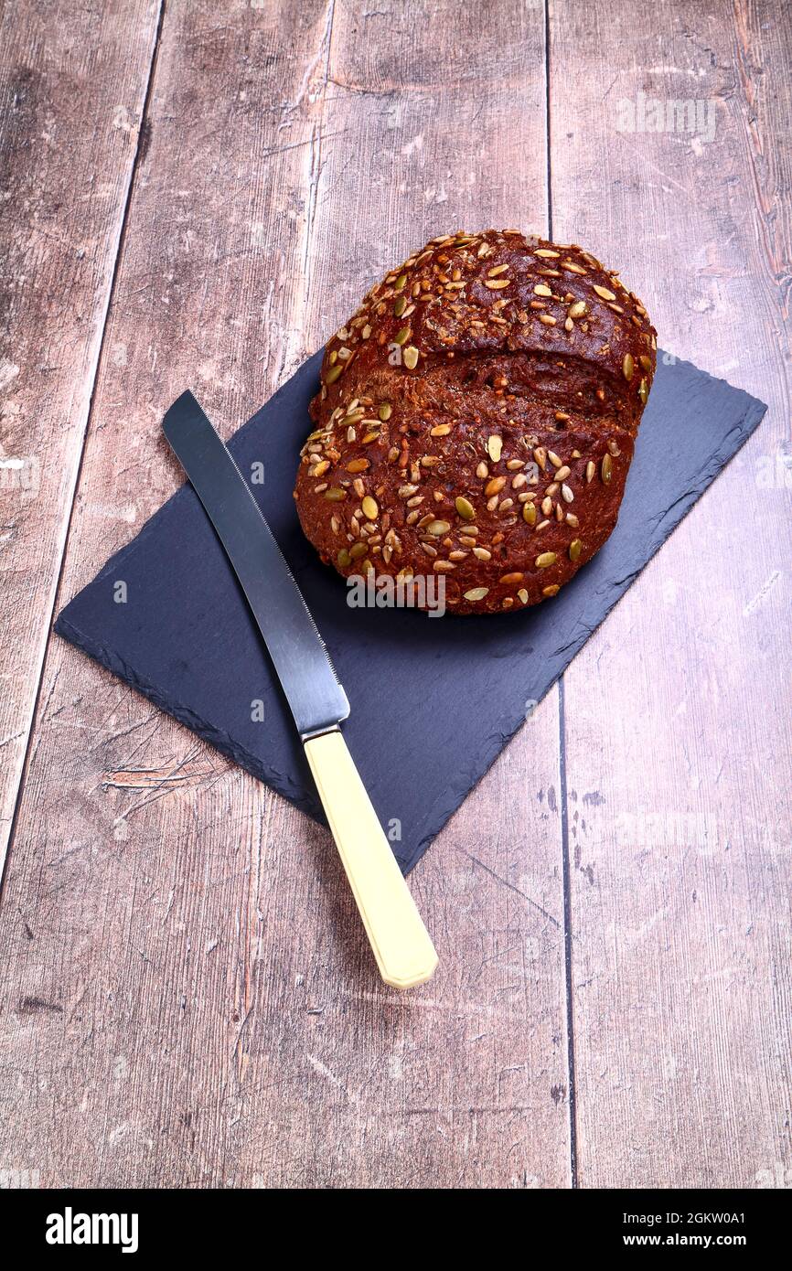 Freshly baked Pumpernickel Boule artisan bread  laid on a wooden table with a old bred knife Stock Photo