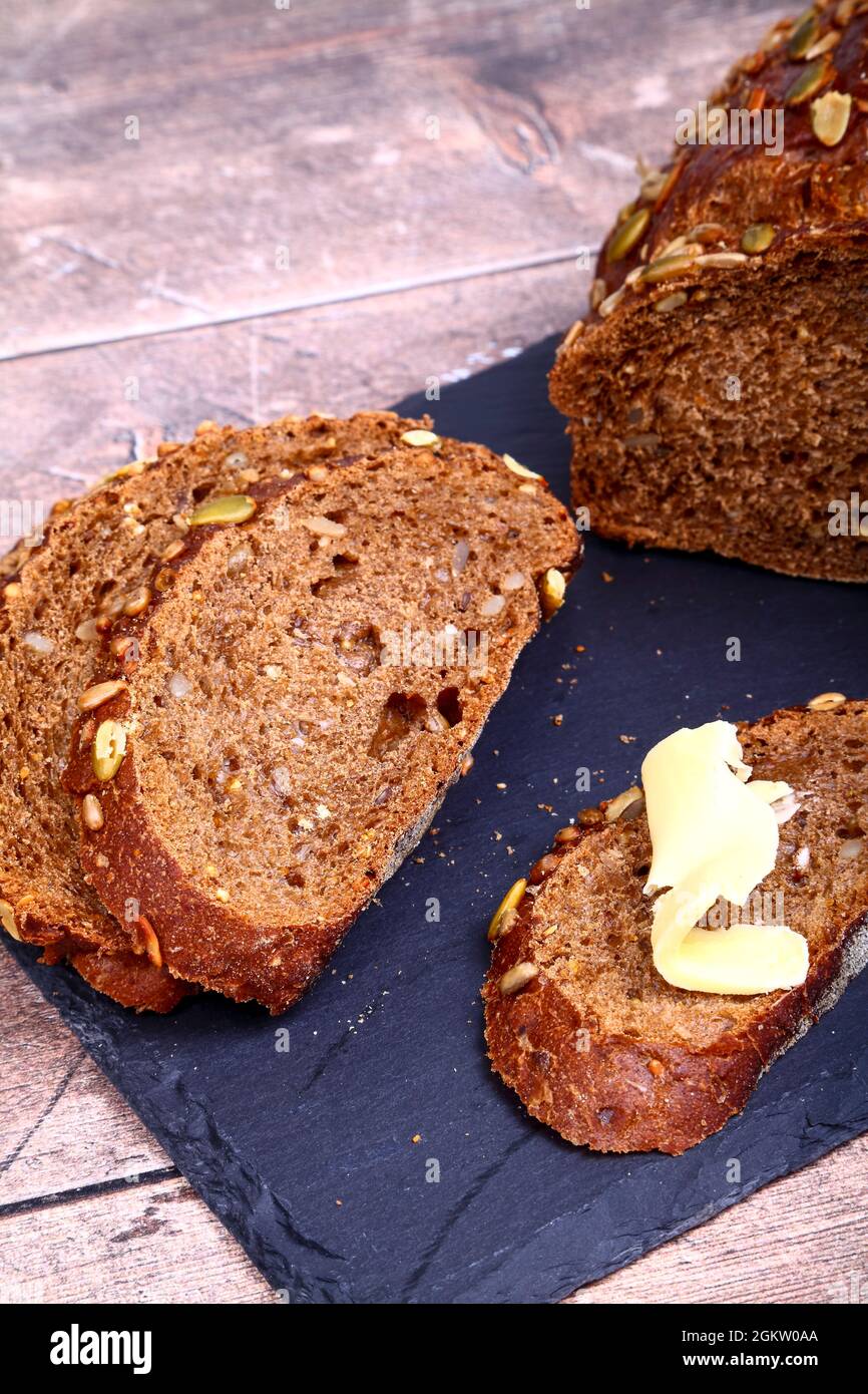 Freshly baked Pumpernickel Boule artisan bread with buttered bread slices cut and laid on a slate serving platter Stock Photo