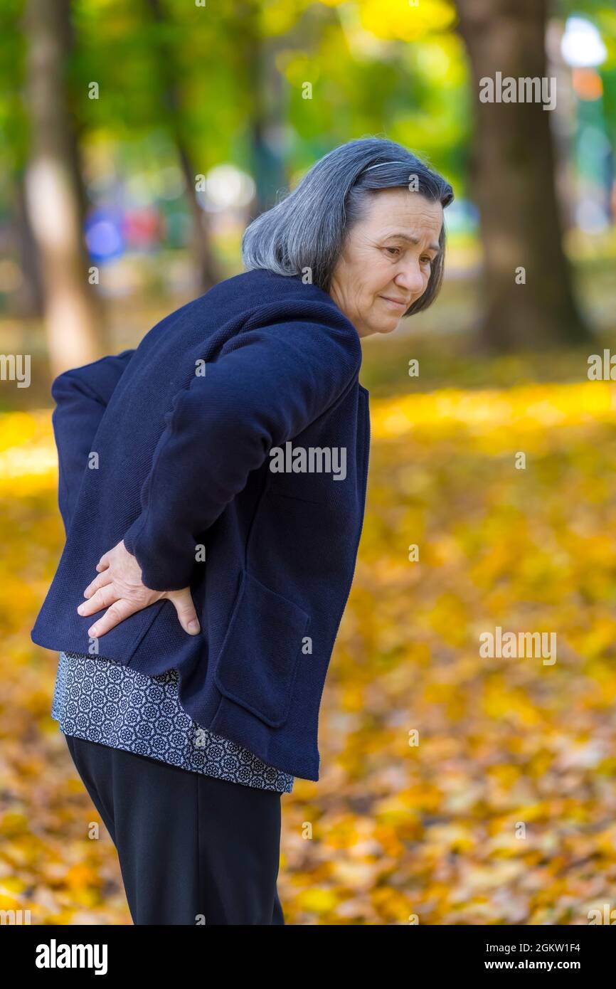 Senior woman suffering from backache outdoors in autumn park. Stock Photo