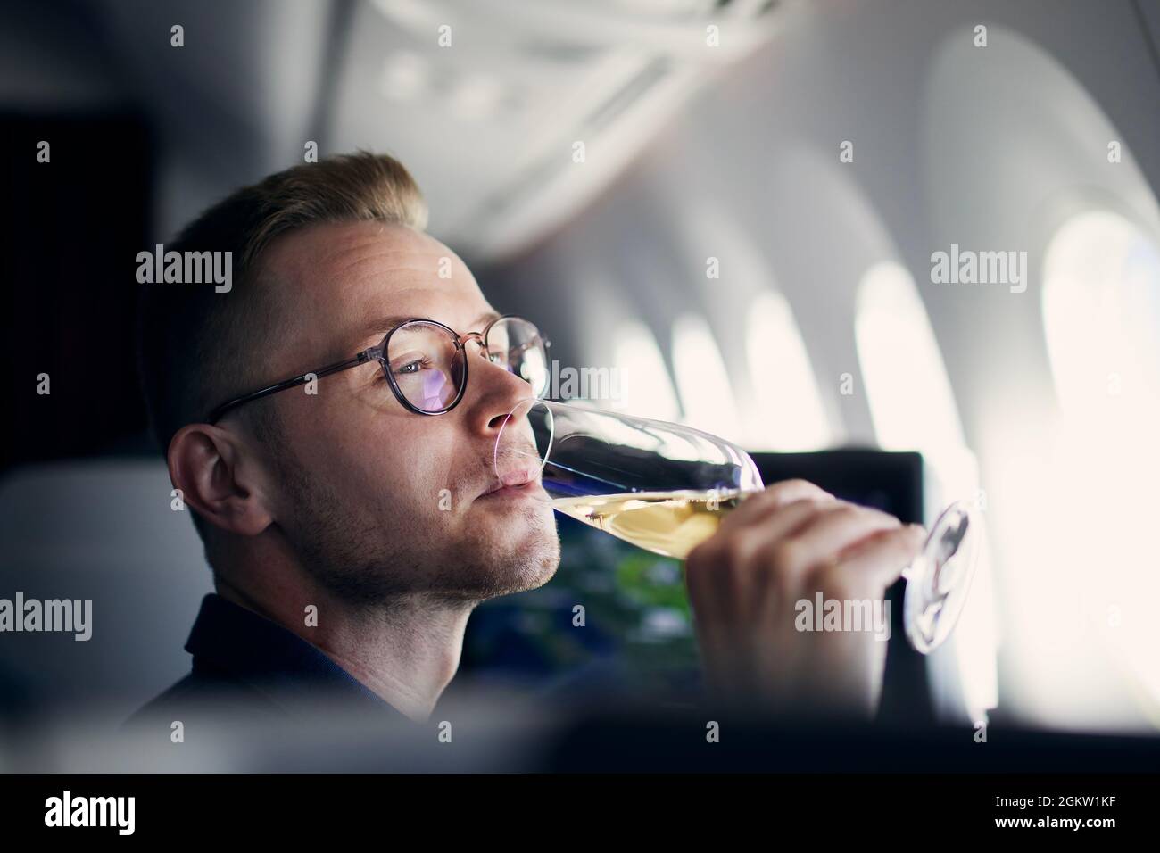 Business travel by airplane. Man looking through window and drinking champagne during flight. Stock Photo