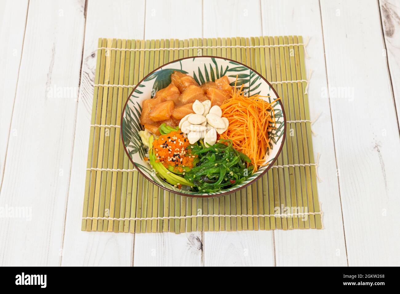 Poke bowl in a super cool container on a bamboo rack with fish roe, marinated salmon, lots of grated carrots, rolled avocado, wakame seaweed salad and Stock Photo